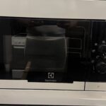 En vit mikrovågsugn från Electrolux med svart glasdörr och reglage syns på en köksbänk. En persons spegelbild syns i mikrovågsugnens dörr.
