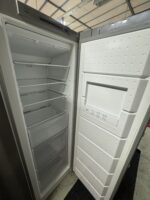 En öppen, tom frysskåp med flera hyllor och lådor inuti. Dörrens insida syns också, där man kan se en kontrollpanel och en vit yta med struktur.